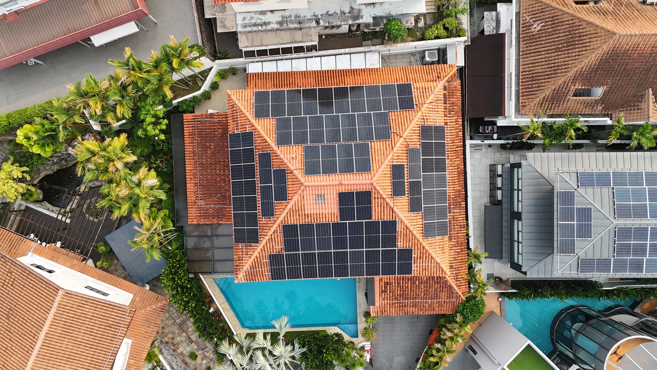 Drone view straight down onto a detached house in Bukit Timah, panels on every face of its terracotta hip roof, pool beside it