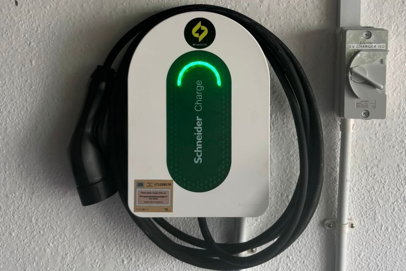 Schneider Charge wall charger installed on a textured wall, its cable coiled round it and the isolator switch beside it