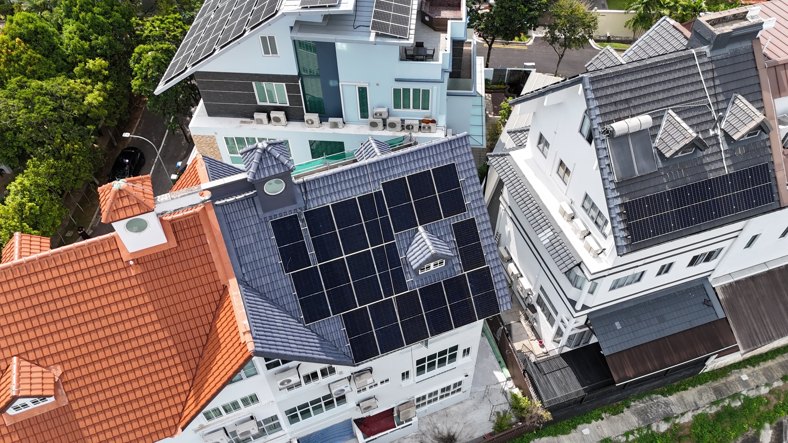 Drone view of a detached house from the street side, panels on the front and side faces of its grey tiled roof