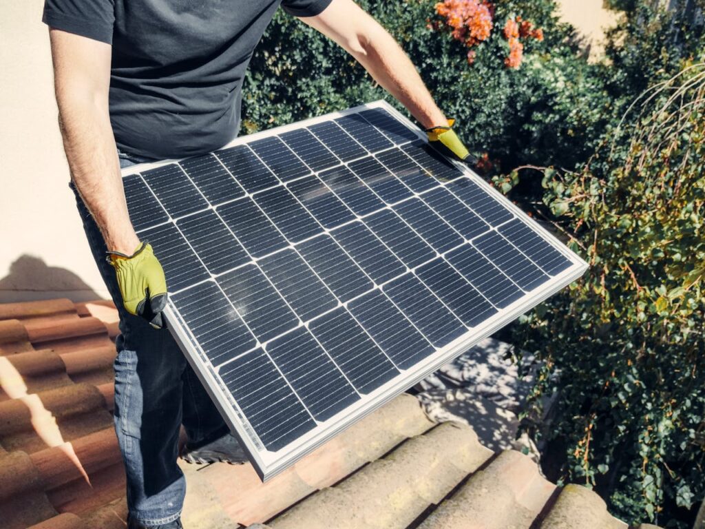 a-person-in-black-shirt-holding-a-solar-panel-while-standing-on-the-roof-9875441 A Person in Black Shirt Holding a Solar Panel while Standing on the Roof